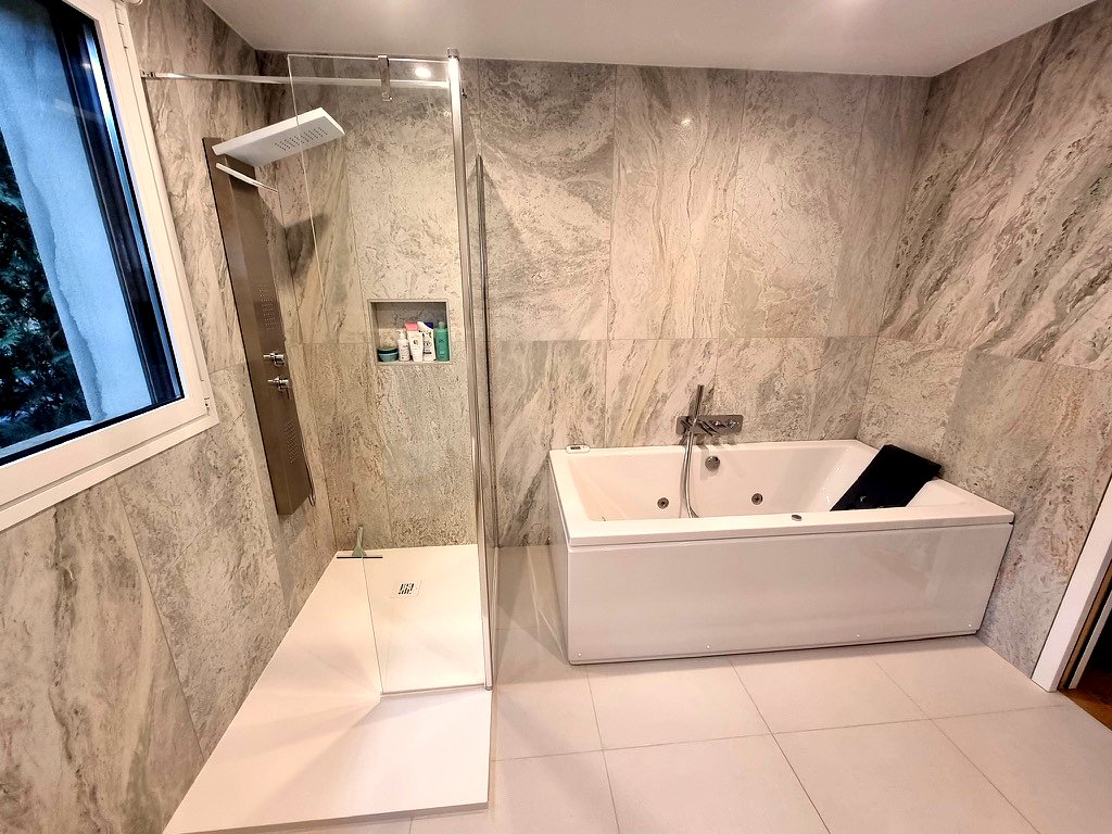 Salle de bains en grand format effet marbre avec baignoire balnéo et douche à paroi fixe, à Fontenay-aux-Roses.