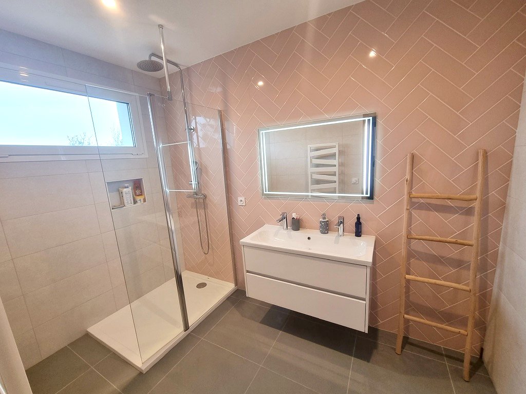 Salle de douche avec faïence rose posée en chevrons, douche à l'italienne et meuble vasque suspendu.