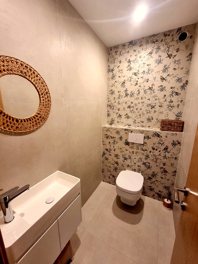 WC suspendu avec lave-mains et carrelage décor oiseaux sur le mur du fond.